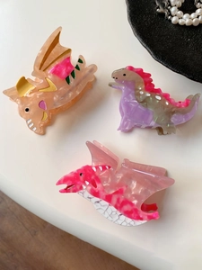 Vue détaillée de trois pinces à cheveux dinosaures en acétate avec texture marbrée