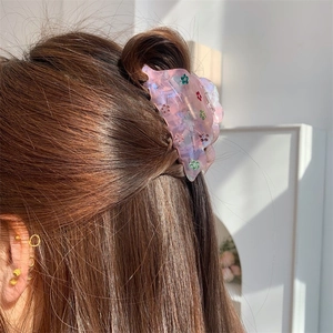 Pince à cheveux fleurie en acétate rose avec strass portée élégamment sur cheveux relevés
