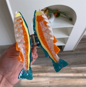 Detail view of a colorful fish-shaped acetate hair claw clip with a strong metal spring