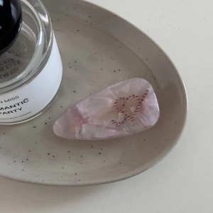 Détail de la pince à cheveux en acétate rose marbré avec cœur en strass sur plateau