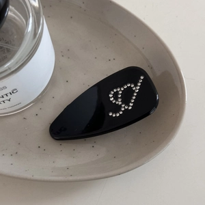 Vue détaillée d'une pince à cheveux goutte noire brillante ornée d'une lettre D en strass