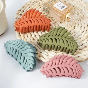 Set of four matte leaf-shaped hair claws in pastel colors on a natural woven mat