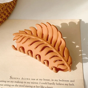 Detail of leaf-shaped hair claw in matte orange finish with artistic leaf shadows