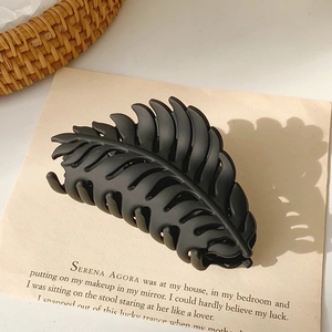 Detail view of large matte black leaf-shaped hair claw clip on minimalist paper background