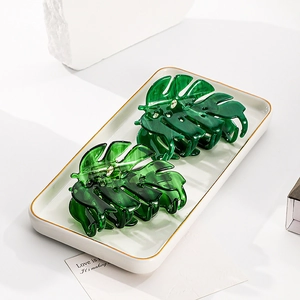 Dettaglio di due mollette per capelli a foglia verde scuro con strass su vassoio ceramica