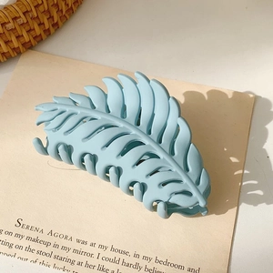 Detail of matte blue leaf-shaped hair claw clip on beige aesthetic background