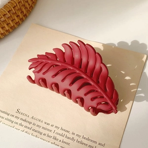 Detailed close-up of a matte burgundy leaf-shaped hair claw clip on a stylish background