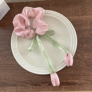 Détail d'un chouchou tulipe en satin rose avec ruban vert sur une assiette blanche