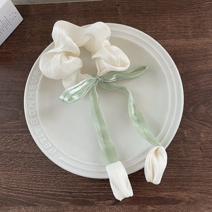 Vue détaillée du chouchou tulipe crème avec ruban vert sur une assiette en porcelaine