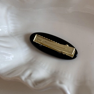 Detailed view of the sleek black oval hair clip with gold metal duckbill clamp design