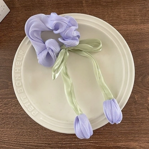 Détail d'un chouchou lavande en soie avec breloques tulipes dans un plateau céramique