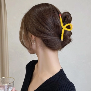 Détail d'une pince à cheveux jaune en forme de crayon sur les cheveux bruns d'une femme