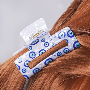Detail view of white PVC hair claw clip with blue evil eye pattern on brown hair