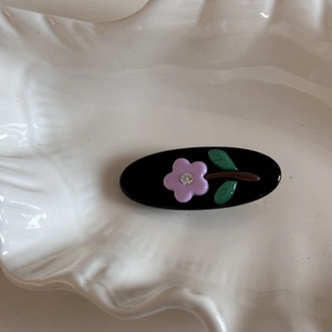 Close-up of black oval hair clip with purple floral patterns and crystal detail