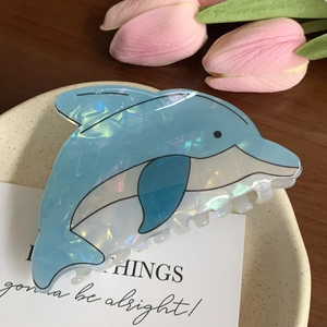 Close-up of a blue dolphin hair claw clip with pearlescent texture on a ceramic tray