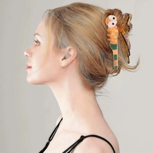 Detailed side view of a large orange acetate dragonfly hair claw clip worn on a bun