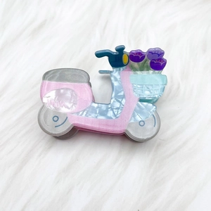 Vue détaillée d'une pince à cheveux rose en forme de Vespa avec tulipes sur fond en peluche
