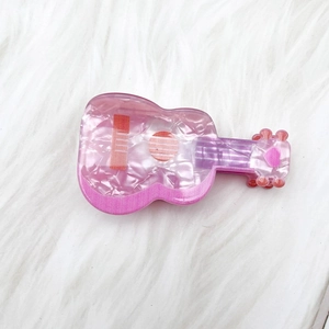 Détail d'une pince à cheveux rose en forme de guitare en acétate avec texture marbrée
