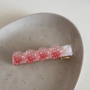 Dettaglio di fermagli per capelli a fragola rosa con pois su base in metallo dorato