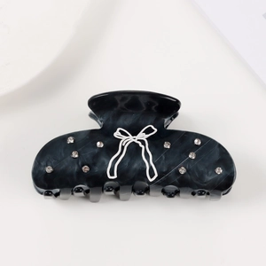 Detail of black marble acetate hair claw clip with crystal rhinestones and bow patterns