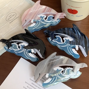 Set of four dolphin-shaped acetate hair claws in various colors on a wooden surface