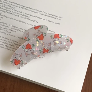 Gros plan d'une pince à cheveux rose nacré avec motif chat sur un livre ouvert