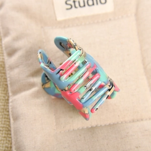 Detail of multi-colored acetic acid hair claw clip with ink pattern on a beige fabric bag