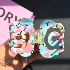 Detail of colorful floral acetate hair claw clip with golden spring held by hand