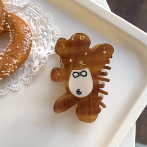 Détail de la pince à cheveux ours marron ambré avec paillettes dorées sur un plateau en dentelle