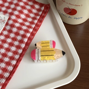 Detail view of yellow acrylic pencil-shaped hair clip with glossy pearl finish on white tray