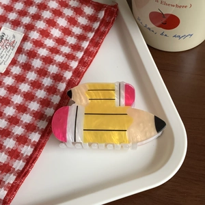 Detail view of yellow acrylic pencil hair claw clip on a white tray with lifestyle decor