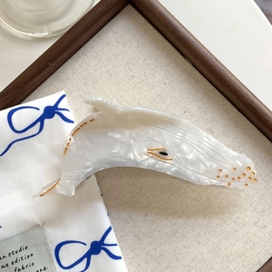 Macro detail of whale-shaped acetate hair claw with pearlescent white marble texture