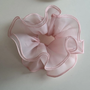 Detailed macro view of the light pink organza fabric texture on a ruffled hair scrunchie