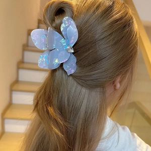 Detail of blue iridescent floral hair claw clip on model's hair with rhinestone accent