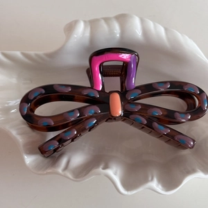 Macro detail of tortoiseshell bow hair claw with purple dots on a ceramic shell tray