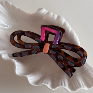 Bow-shaped tortoise hair claw clip with colorful polka dots on a white shell tray