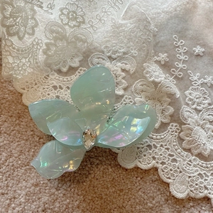Detail of light blue floral hair claw clip with pearlescent finish and crystal drop