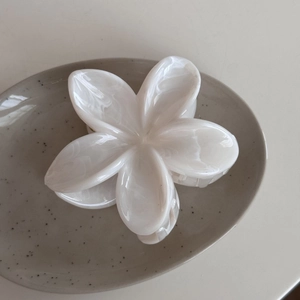 Close-up of white acetate flower hair claw clip with elegant marble texture on a ceramic plate