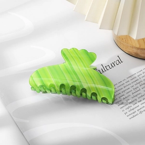 Detail view of light green gradient hair claw clip with vertical stripes on a white magazine