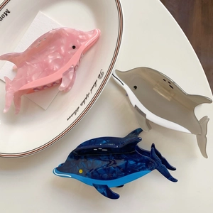 Trois pinces à cheveux dauphin en acétate rose, beige et bleu sur une assiette blanche