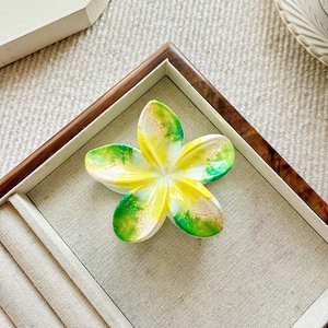 Top view of a plumeria flower hair claw with marble texture on a linen jewelry tray