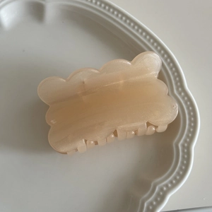 Detail of champagne wavy biscuit hair claw clip with fine glitter in white porcelain dish