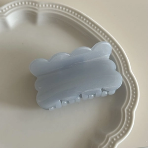 Macro shot of a light blue wavy hair claw clip with pearlescent resin finish in a white plate
