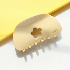 Détail d'une pince à cheveux jaune crème en forme de fleur avec gravure décorative