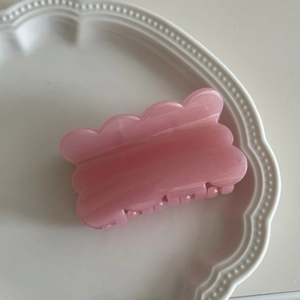 Macro detail of pink pearlescent wavy hair claw clip displayed on a white ceramic tray