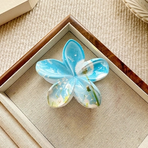 Detail shot of a blue floral hair claw clip with dandelion print in a wooden tray