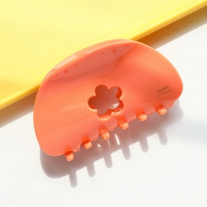 Détail d'une pince à cheveux orange corail en acétate avec un motif floral ajouré