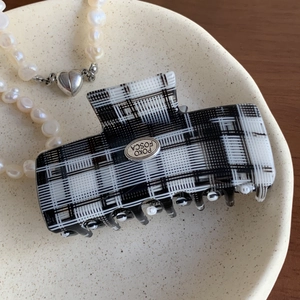 Detailed macro view of black and white checkered acetate hair claw with silver metal logo tag