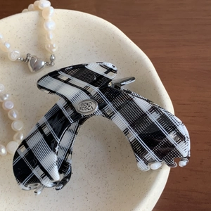 Detail of checkered acetate hair claw clip with silver metal logo plate on a tray