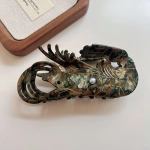 Detailed close-up of lobster-shaped acetate hair claw with pearl and tortoiseshell texture